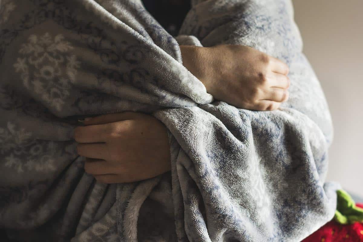 Foto mostra pessoa se agasalhando com cobertor durante o frio.